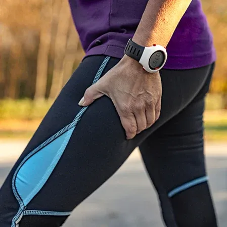 A woman in athletic clothing holding her leg in pain from sciatica